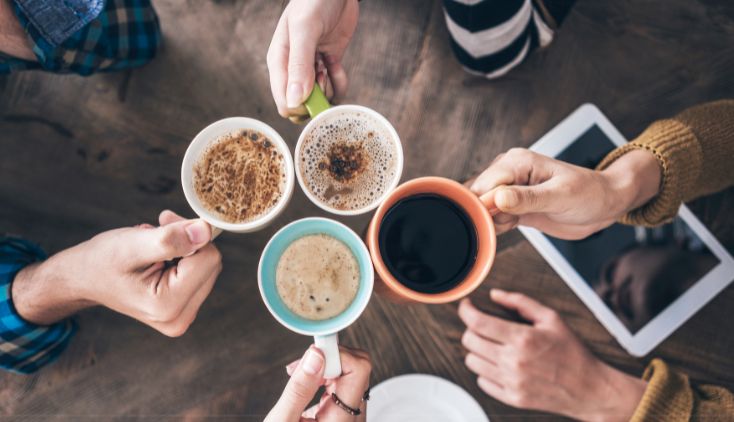 A top-down view of four people holding mugs of coffee and lattes together.