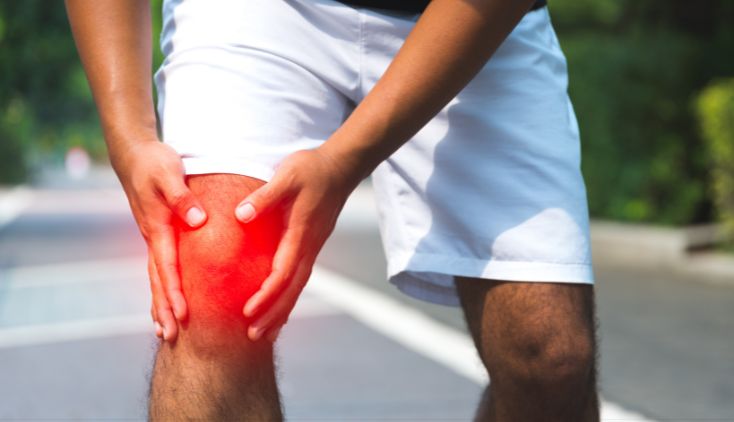 A close up of a man holding his knee, which has a red light over it as if in pain.